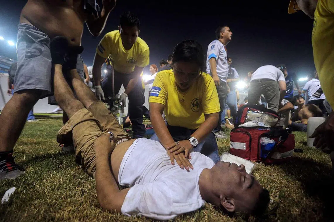 TOPSHOT - Rescuers attend an injured man lying on the pitch following a stampede during a football match between Alianza and FAS at Cuscatlan stadium in San Salvador, on May 20, 2023. Nine people were killed May 20, 2023 in a stampede at an El Salvador stadium where soccer fans had gathered to watch a local tournament, police said. (Photo by Milton FLORES / AFP)
