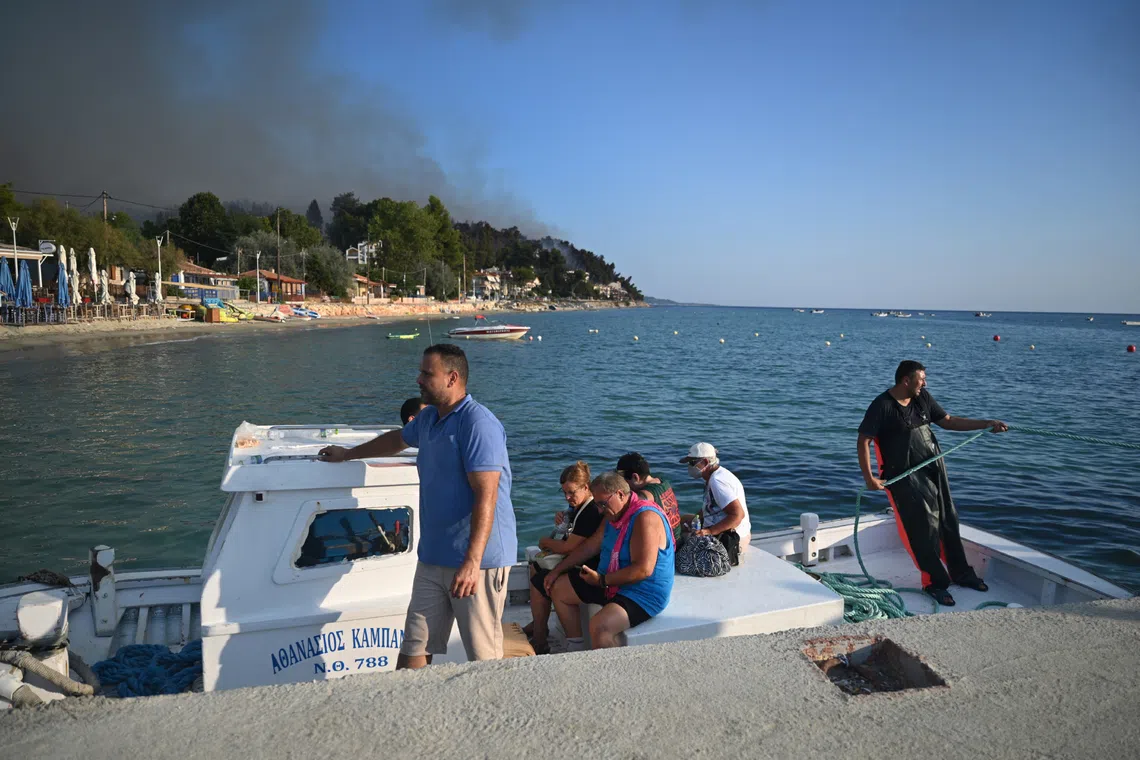 Residents and holidaymakers are transported by boats during a wildfire in Siviri, Halkidiki, Northern Greece, on Aug 13.