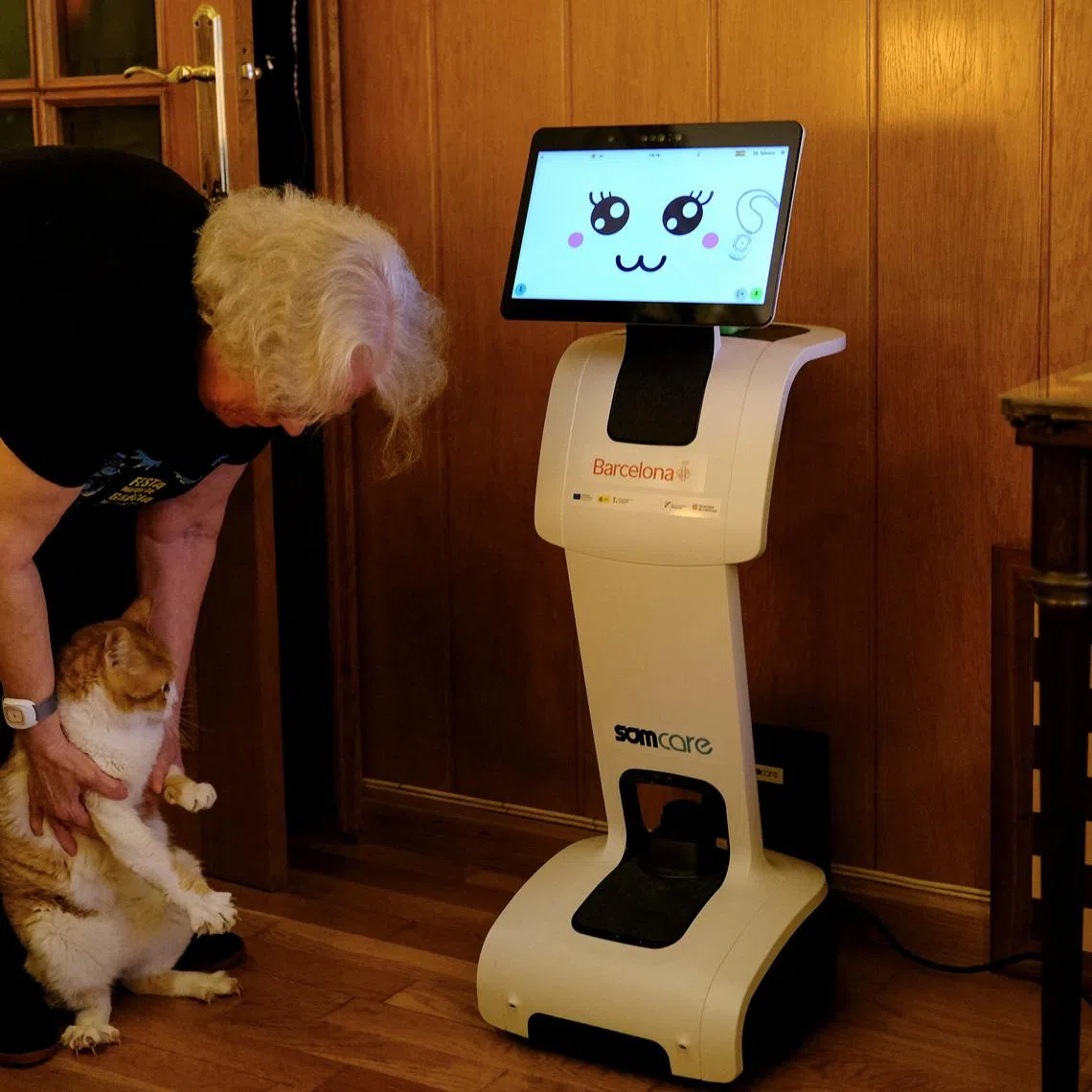 Irene Veglison, 67, holds her cat named Sweet, net to her robot, nicknamed \"Sandi\", inside her apartment, where she lives with two cats and her robot, during a pilot project to improve tele-assistance, to provide support to those experiencing the early stages of cognitive decline, in Barcelona, Spain, February 26, 2026. REUTERS/Nacho Doce