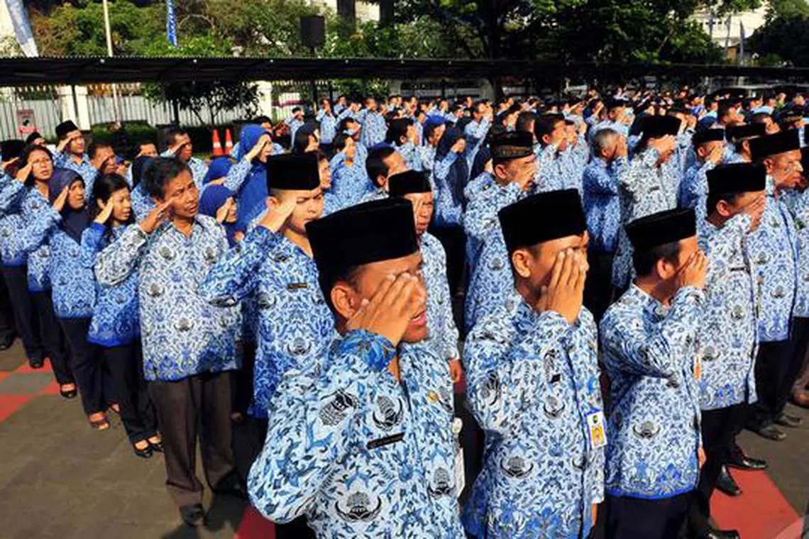 Civil servants in Jakarta saluting the flag while singing the national anthem during a ceremony (no date).  Government workers are facing work disruptions following big budget cuts.
