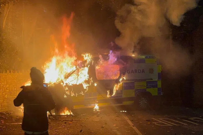 Onlookers film a police vehicle burning as a protest outside a hotel housing asylum seekers turns violent in Saggart, south-west of Dublin in Ireland on Oct 21.