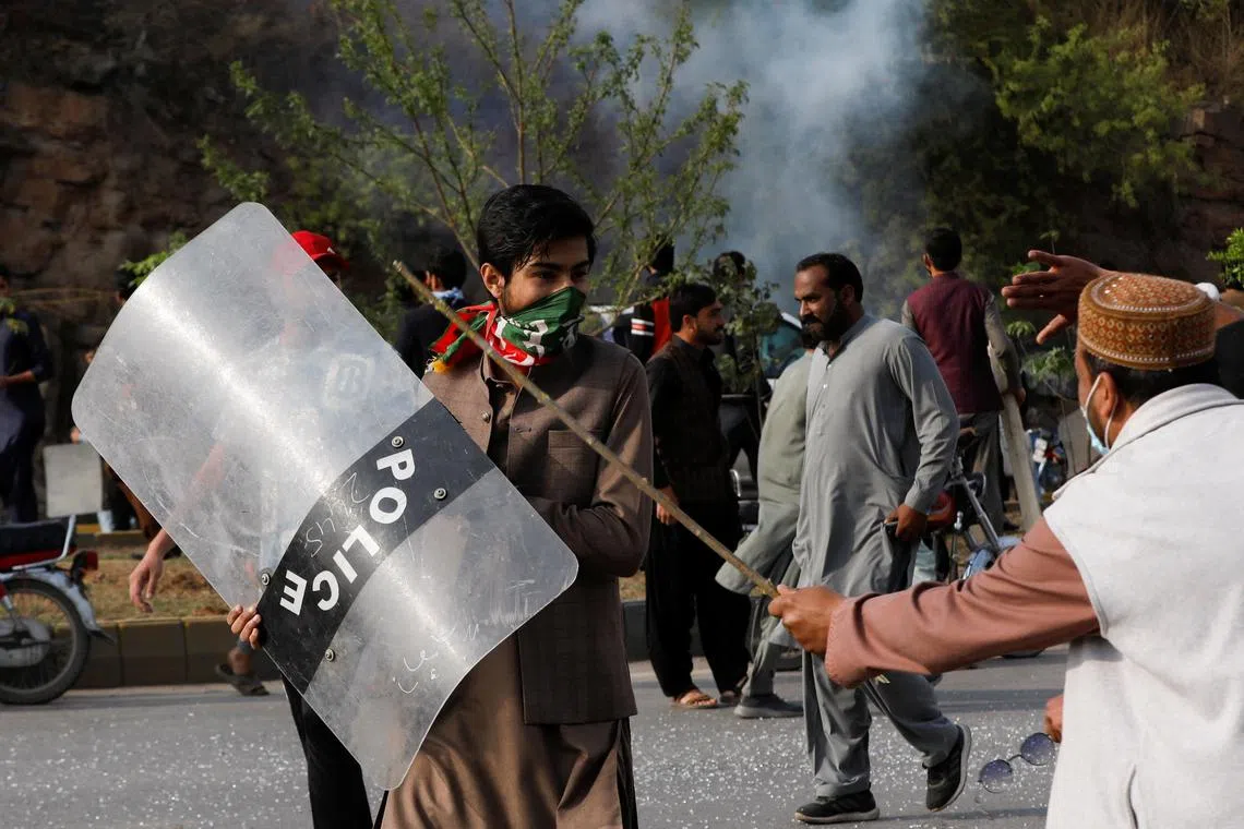 A supporter of former Pakistani Prime Minister Imran Khan, walks with a riot shield used by the police, during a clash outside the federal judicial complex in Islamabad on March 18, 2023.  
