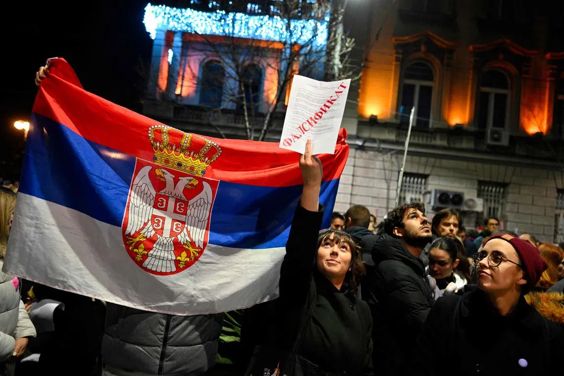 Protesters holding a Serbian flag and a mock ballot paper reading "forgery" rally outside the Electoral Commission building in Belgrade.
