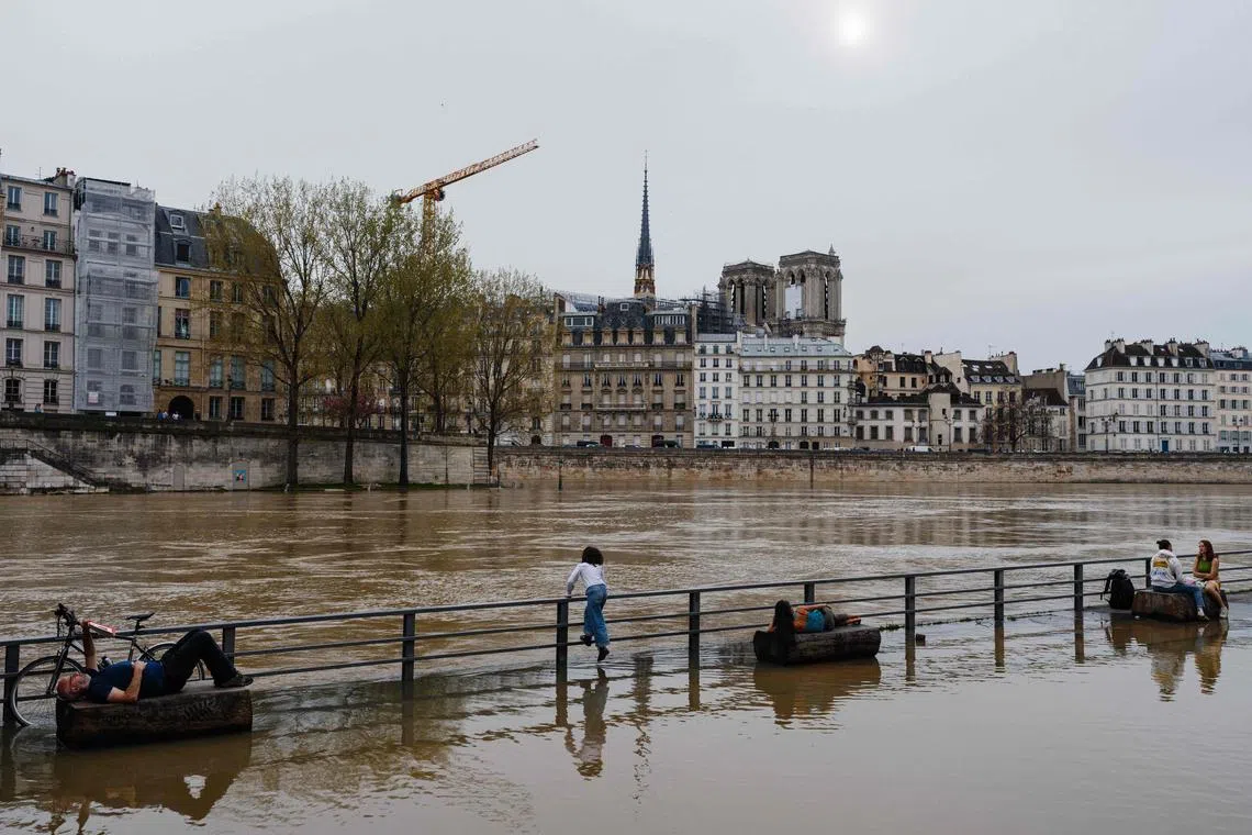 People enjoy the warm weather at the flooded docks along the Seine river in Paris on April 6, 2024. 