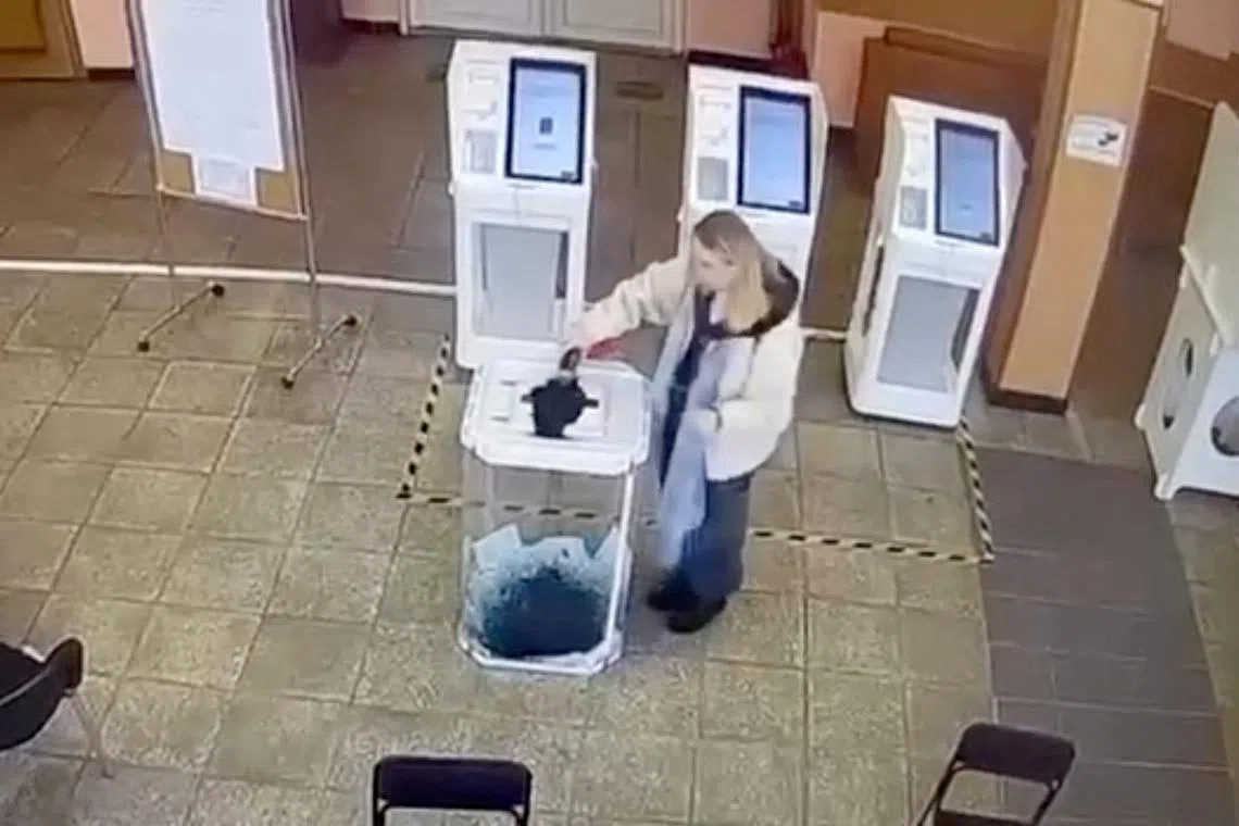 A woman pours a liquid into a ballot box, during the Russian presidential election in Moscow, Russia, in this screen grab taken from a video recording of a screen showing CCTV footage, March 15, 2024. Video obtained by Reuters/via REUTERS