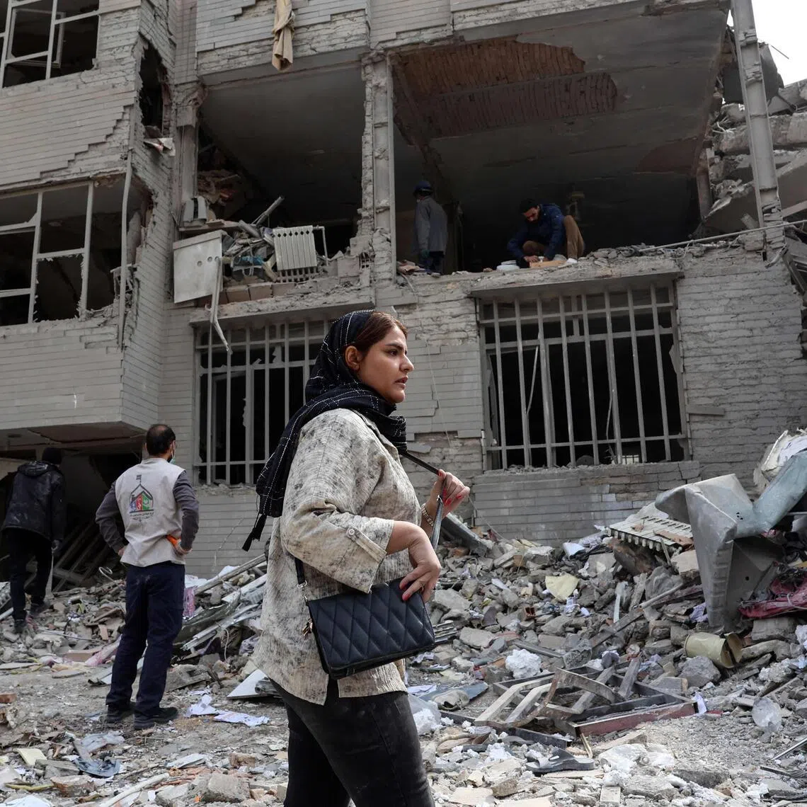 TOPSHOT - A woman stands in front of a destroyed residential building as residents collect their belongings from the rubble in Tehran on March 12, 2026. The United States and Israel started striking Iran on February 28, killing the Iranian supreme leader and top military leaders, and prompting authorities to retaliate with strikes on Israel and across the Gulf. (Photo by AFP) / 