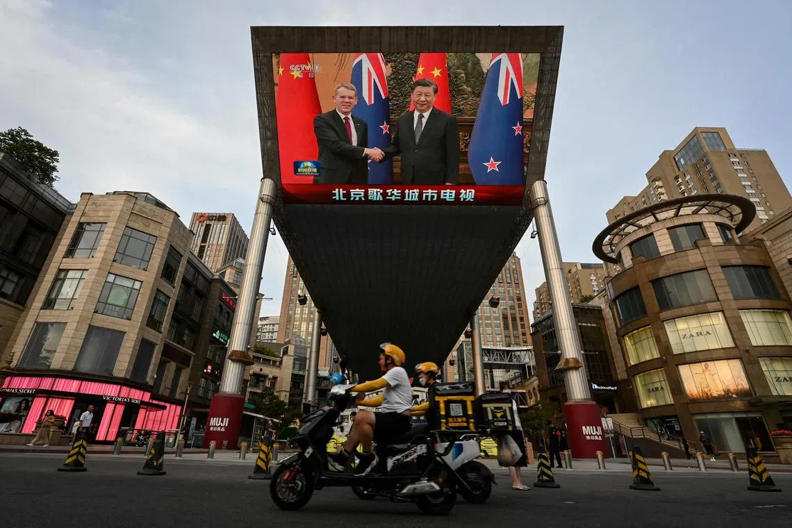 An outdoor screen shows news coverage of New Zealand's Prime Minister Chris Hipkins meeting with China's President Xi Jinping.
