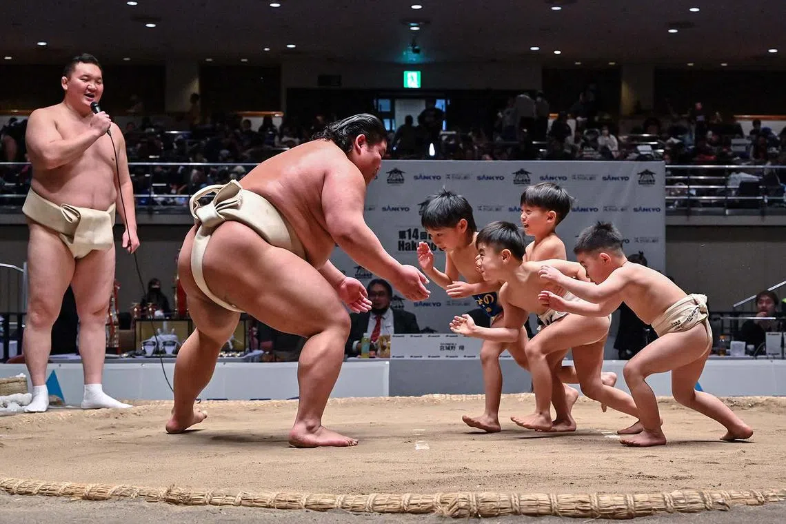 Retired Mongolian-born "yokozuna" wrestler Hakuho (far left), who now goes by the name Miyagino, watches as participants (right) try to push out Japanese wrestler Hakuoho (left) during a sumo class for youngsters on the sidelines of the 14th Hakuho Cup, a competition for young sumo wrestlers from elementary and middle school, at the Kokugikan arena in the Ryogoku area of Tokyo on Feb 12, 2024. 