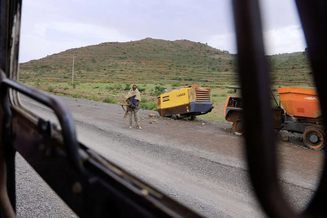 A Tigrayan Militia member stands next to construction machinery destroyed during the fighting between the Tigray People's Liberation Front (TPLF) and Ethiopian National Defence Force (ENDF) allied with Amhara Special Forces and Eritrean Defence Forces (EDF) on the outskirts of Samre, Tigray Region, Ethiopia, June 23, 2023. REUTERS/Tiksa Negeri