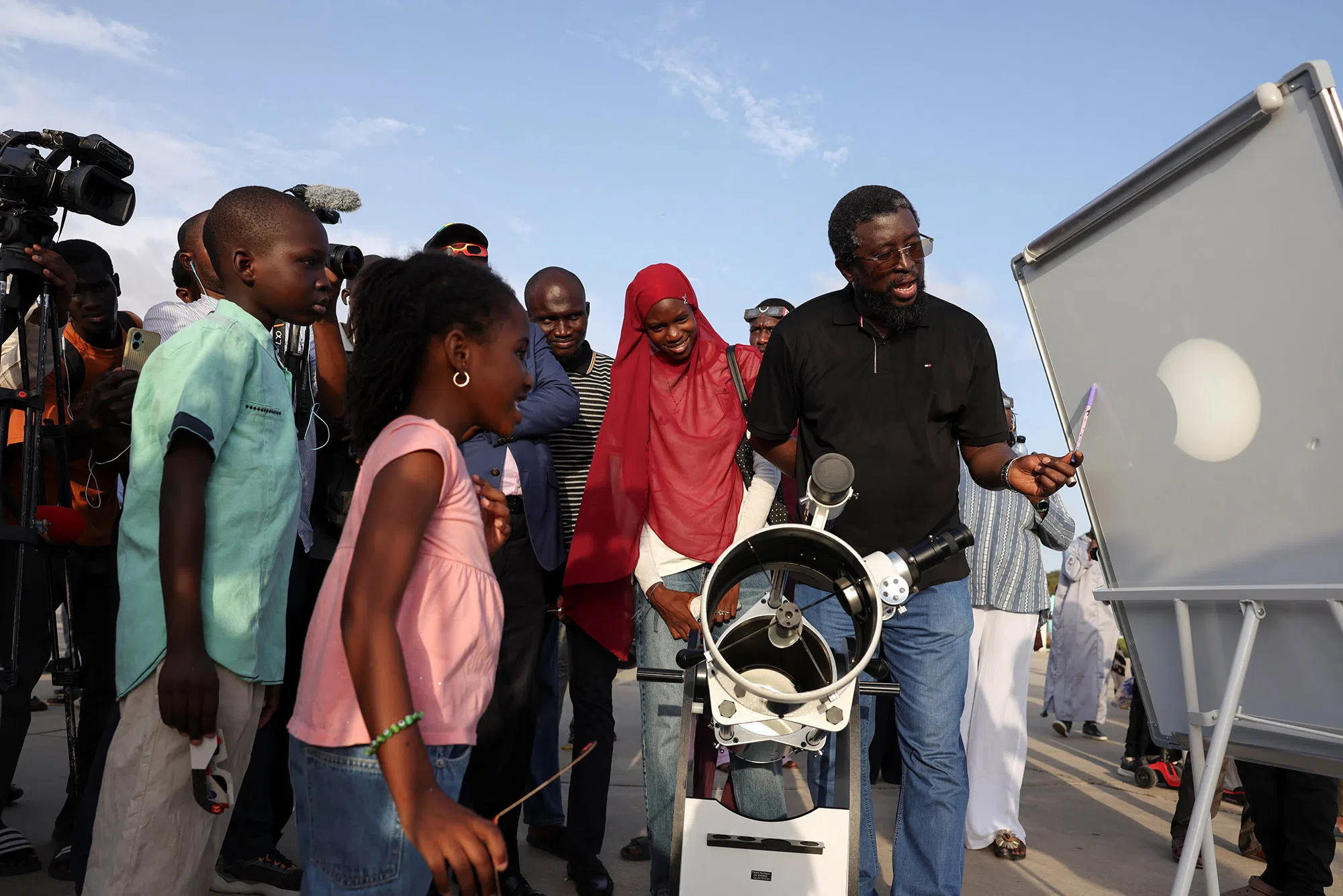 A man projects an image of the sun onto a screen via a telescope with a solar filter as people observe, in Dakar, Senegal, August 12, 2026. REUTERS/Misper Apawu