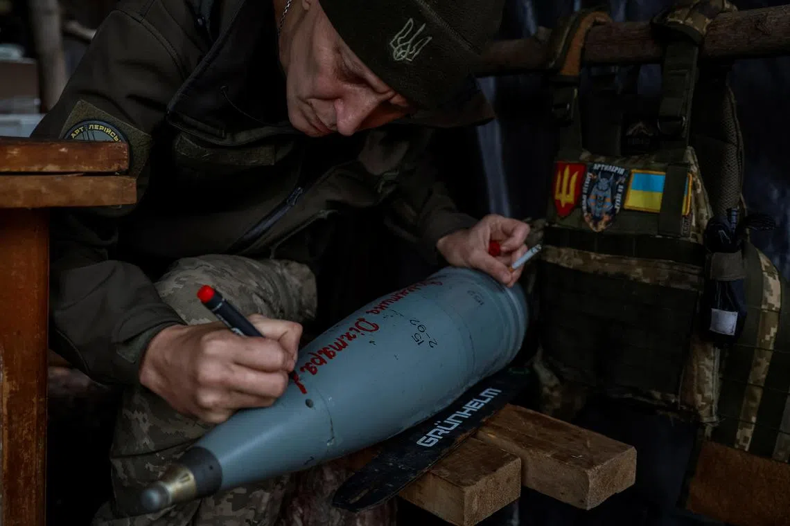 A Ukrainian serviceman writes the name of a soldier killed in action on a howitzer shell, in Ukraine's Donetsk region.