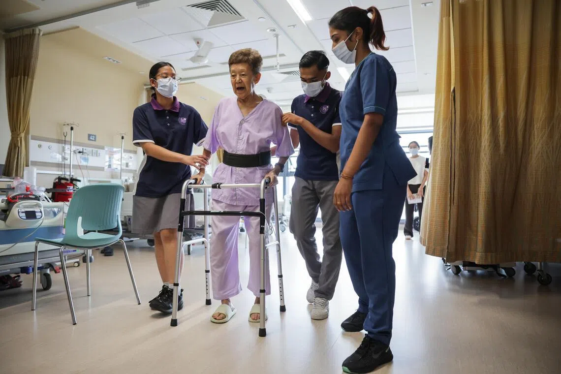 (From left) NorthLight School student Aderes Liv Fadzlin and Sharma Shah Vel Subagar, assists a patient with walking by holding the gait belt during a demonstration, alongside Senior Care Support Associate Netthiya Pandian (right).