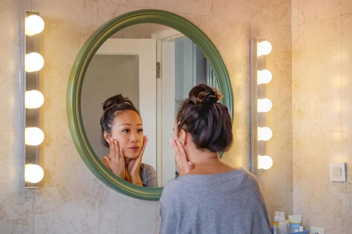 Pretty Asian lady with her hair up looking into the mirror