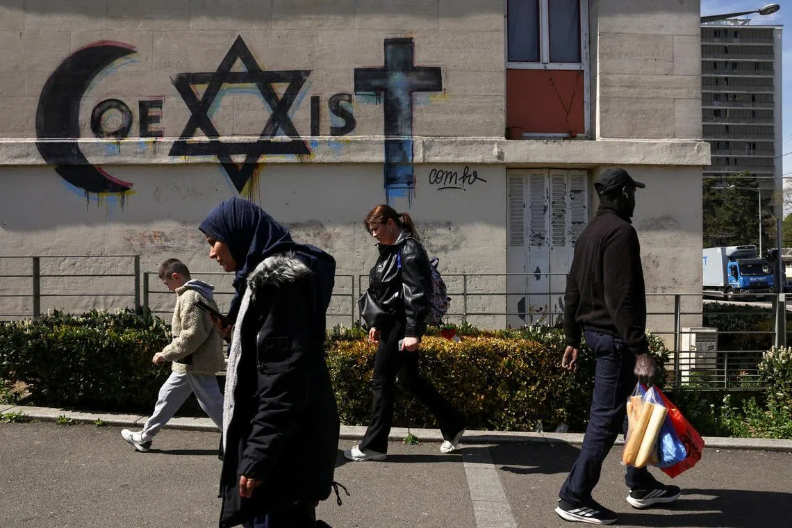 People walk past a mural which reads \"coexist\", made from religious symbols representing the religions of Islam, Judaism and Christianity, near to the market in the Paris suburb of Sarcelles, France, April 14, 2026. REUTERS/Tom Nicholson