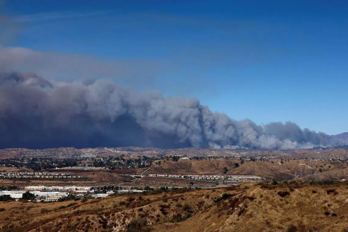 A cloud of smoke from the Hughes Fire rises as firefighters and aircraft battle it near Castaic Lake, as seen from a highway nearby in California on Jan 22, 2025.