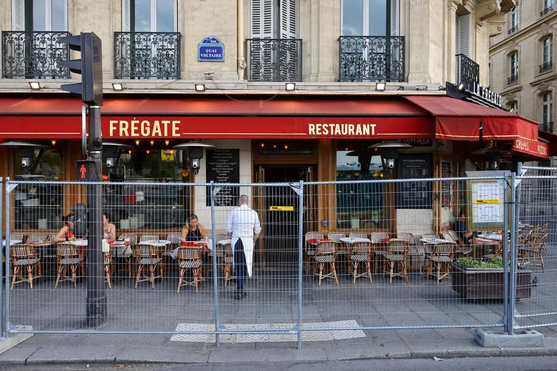 People sit at a restaurant surrounded by empty tables as the security perimeter fence for the opening ceremony is deployed ahead of the Paris 2024 Olympic and Paralympic Games on July 19, 2024.