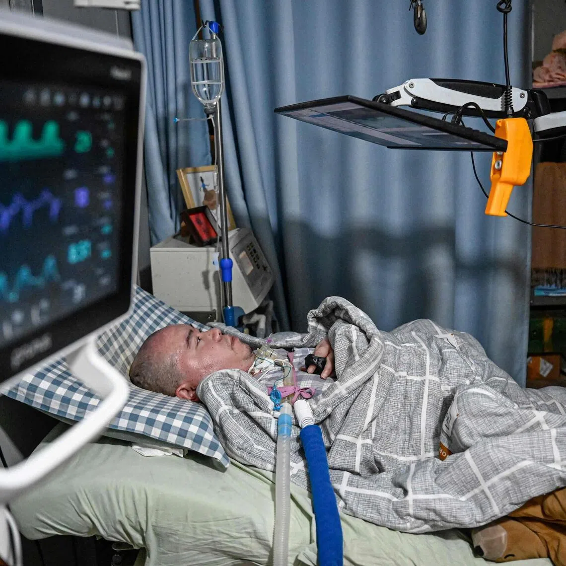 Mr Li Xia, who has Duchenne muscular dystrophy, using a trackball with his fingers to control the computer on a bed at his house.