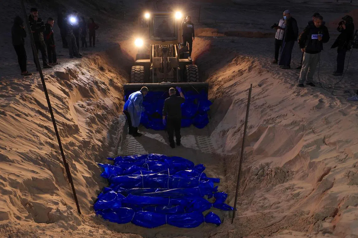 TOPSHOT - The shrouded bodies of Palestinians killed in nothern Gaza, that were taken and later released by Israel, are burried in a mass grave in Rafah, on the southern Gaza Strip on December 26, 2023, amid ongoing battles between Israel and the militant group Hamas. (Photo by Mahmud HAMS / AFP)