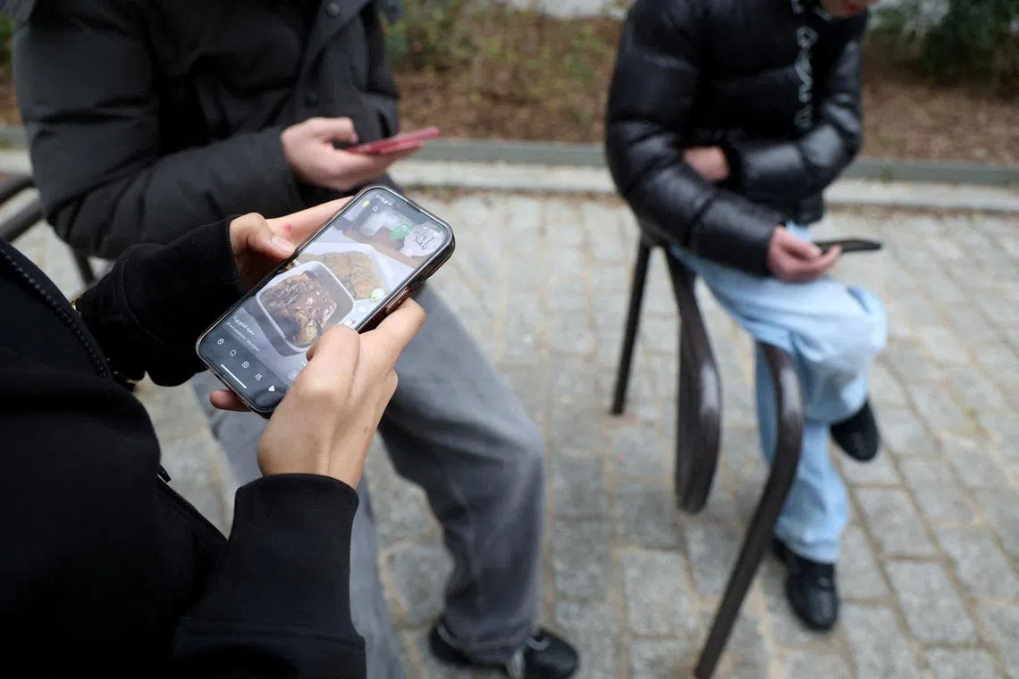 FILE PHOTO: Teenagers look at their mobile phone screens during an interview with Reuters about the bill aimed at banning the use of social networks for those under 15 and mobile phones in high schools from the start of the 2026 school year, in Paris, France, February 20, 2026. REUTERS/Manuel Ausloos/File Photo