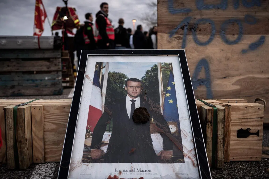 TOPSHOT - A defaced portrait of French president Emmanuel Macron is displayed on the road as unionists block the access to the Blayais Nuclear Power Plant, on March 21, 2023 near Blaye, south-western France, a few days after the government pushed a pensions reform through parliament without a vote, using the article 49.3 of the constitution. - The French government survived two no-confidence motions in parliament on March 20, 2023 but still faces intense pressure over its handling of a controversial pensions reform. (Photo by PHILIPPE LOPEZ / AFP)
