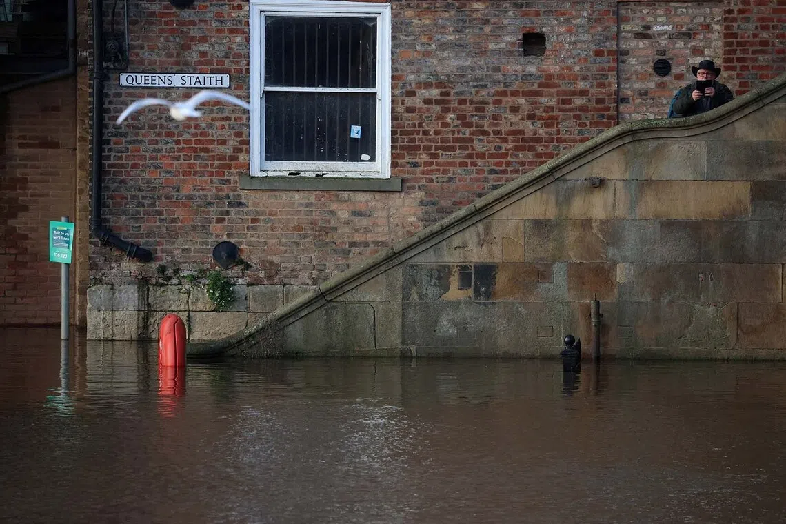 A man using his phone to take photographs of a section of River Ouse, which burst its banks and partially flooded sections of nearby roads, in York, Britain, Dec 10, 2025. 