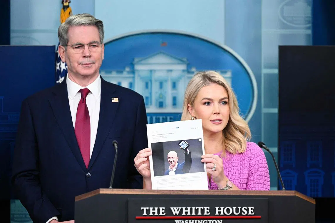 White House Press Secretary Karoline Leavitt, joined by US Secretary of Treasury Scott Bessent, holds a news article on Amazon CEO Jeff Bezos that reads "Amazon partnered with China propaganda arm" during a daily briefing at the White House on April 29.