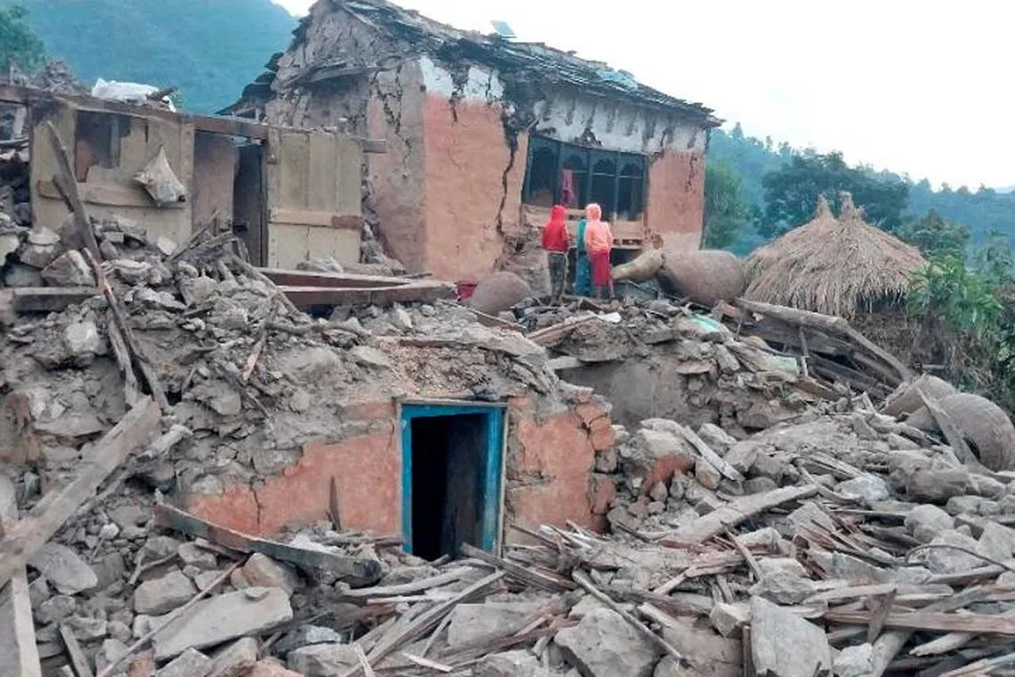 People stand outside the ruins of collapsed houses after an earthquake in Nepal on Nov 9, 2022.