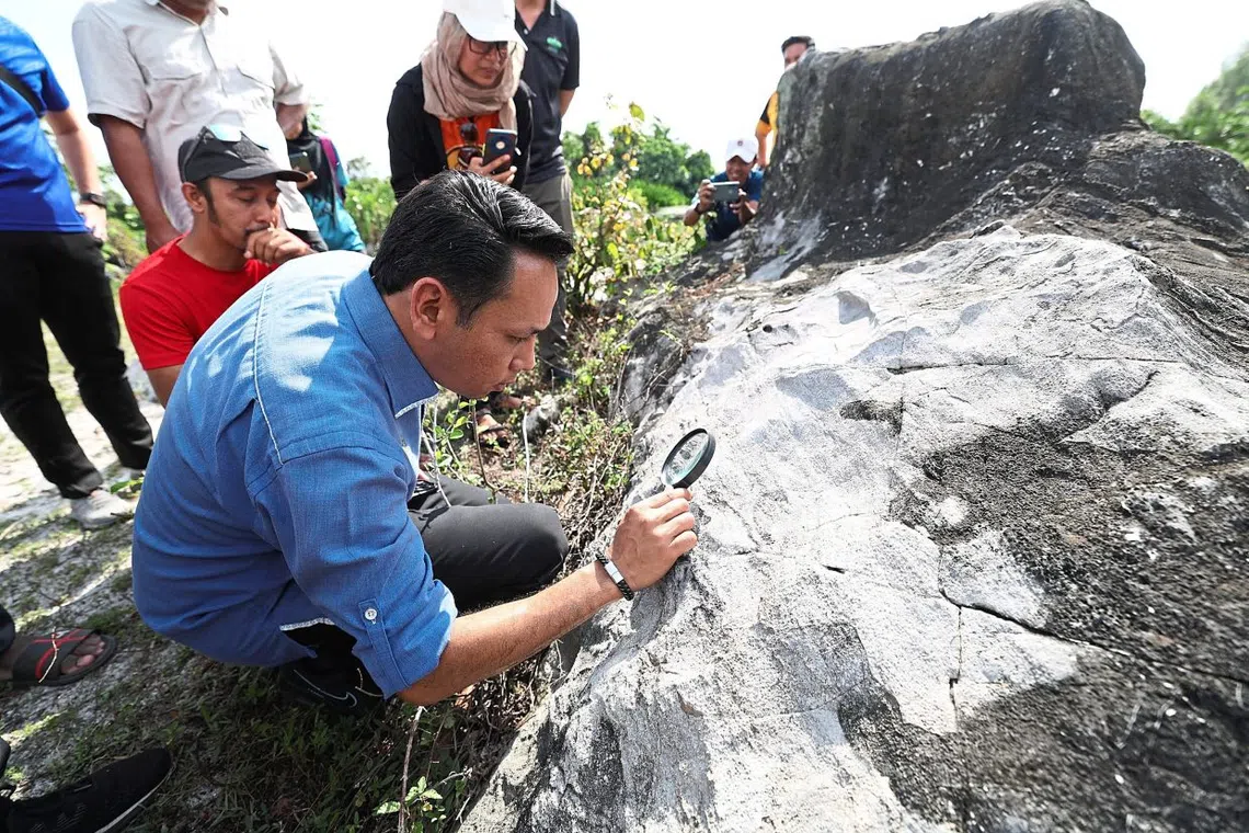 Mohd Azlan Helmi examining fossils attached to rocks during a visit to an area near Kampung Changkat Tualang.