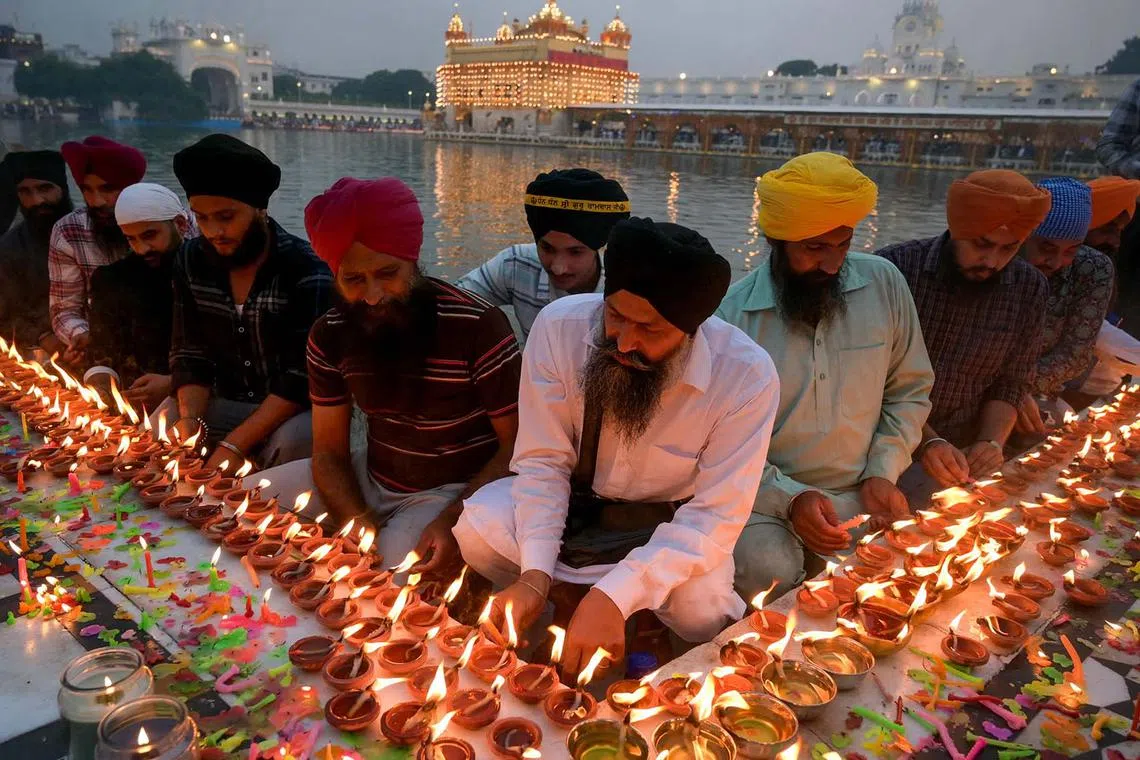 Sikh devotees light candles at the illuminated Golden Temple on the birth anniversary of Sikh Guru Ram Das, in Amritsar on Oct 30.