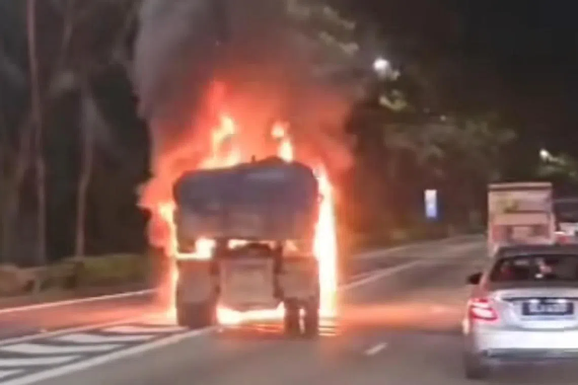 The front of a stationary truck, which is located on the left lane of the road, is seen engulfed in flames.