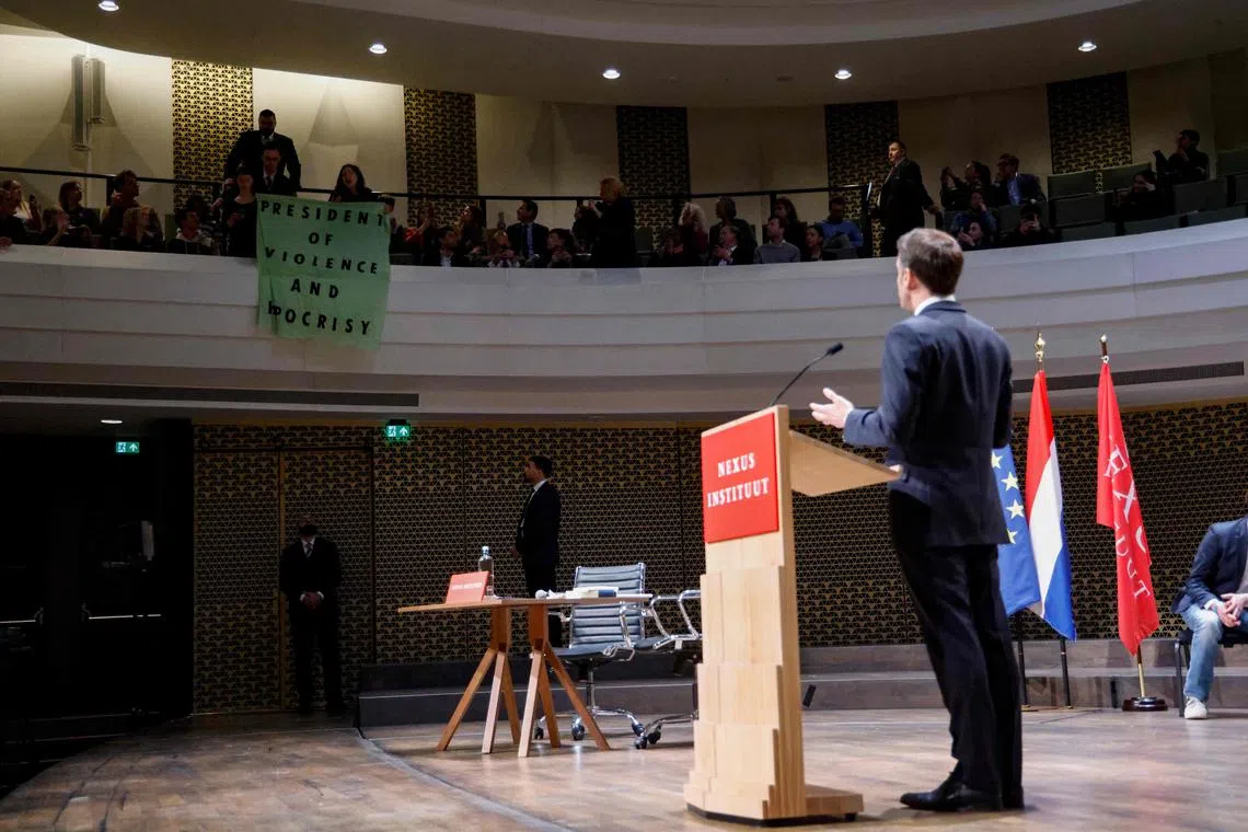 Students hold a banner reading, "President of violence and hypocrisy" during French President Emmanuel Macron's speech to the Nexus Institute.