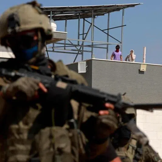 An Israeli soldier standing in front of a Palestinian house in the village of Qusra,  in the occupied West Bank, after rogue settlers blockaded Palestinian homes.