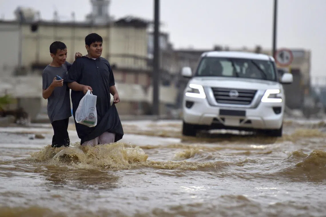 Youthd walk in a flooded street following heavy rains in the Saudi coastal city of Jeddah on November 24, 2022.