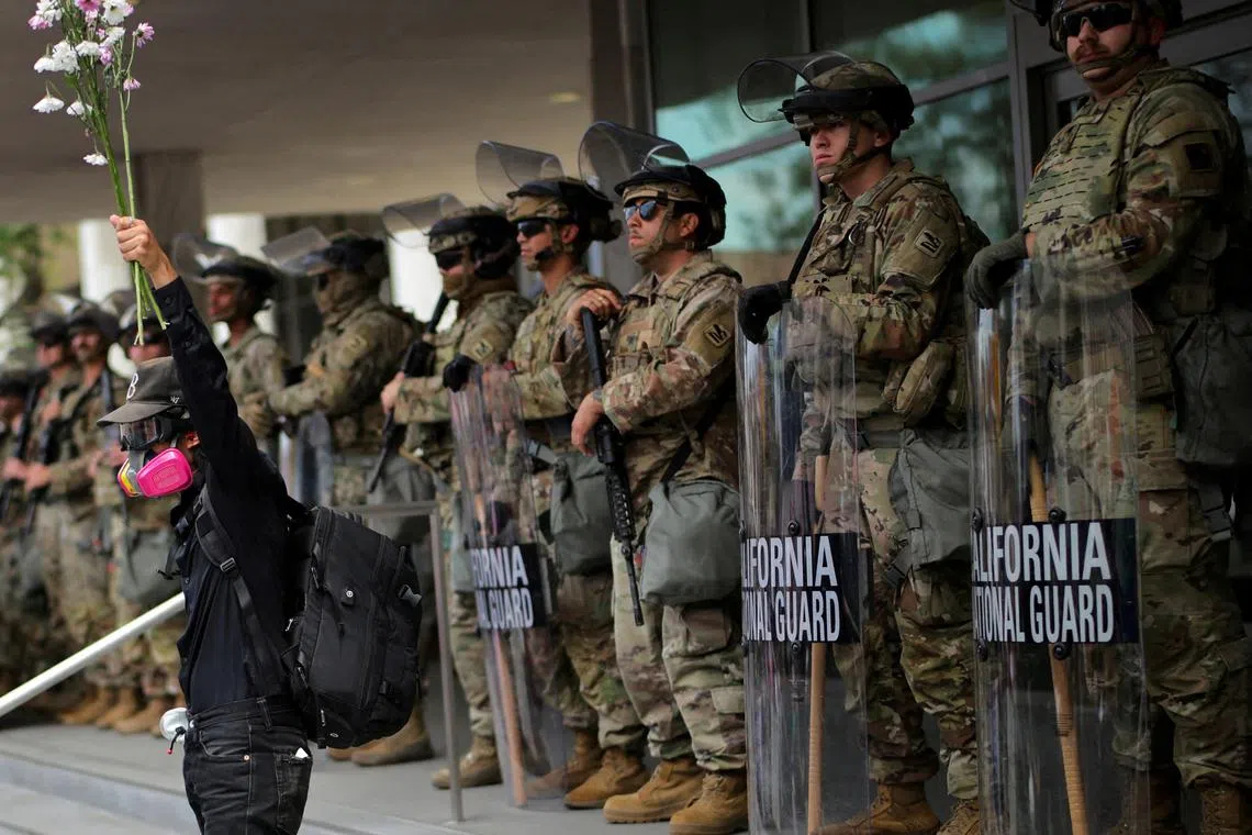 FILE PHOTO: A demonstrator raises his hand holding flowers as members of the National Guard stand in formation outside a federal building during the No Kings protest against U.S. President Donald Trump's policies, in Los Angeles, California, U.S., June 14, 2025.  REUTERS/Daniel Cole/File Photo