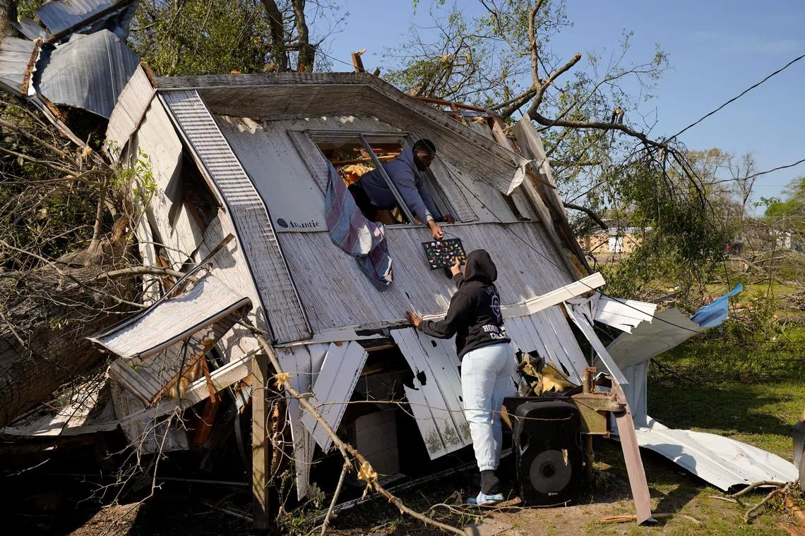 Jeremiah Stapleton, 18, passing a laptop to a family member from the window of his grandfather's home which was crushed by a large tree after thunderstorms spawning high straight-line winds and tornadoes ripped across the state, in Rolling Fork, Mississippi, U.S. March 26.