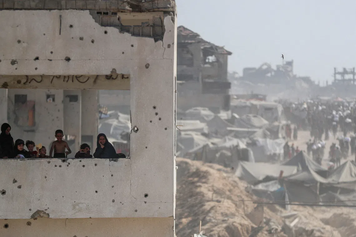Women and children look out from a damaged building as Palestinians carry aid supplies that entered Gaza through Israel, in Beit Lahia, northern Gaza Strip, August 2, 2025. REUTERS/Mahmoud Issa