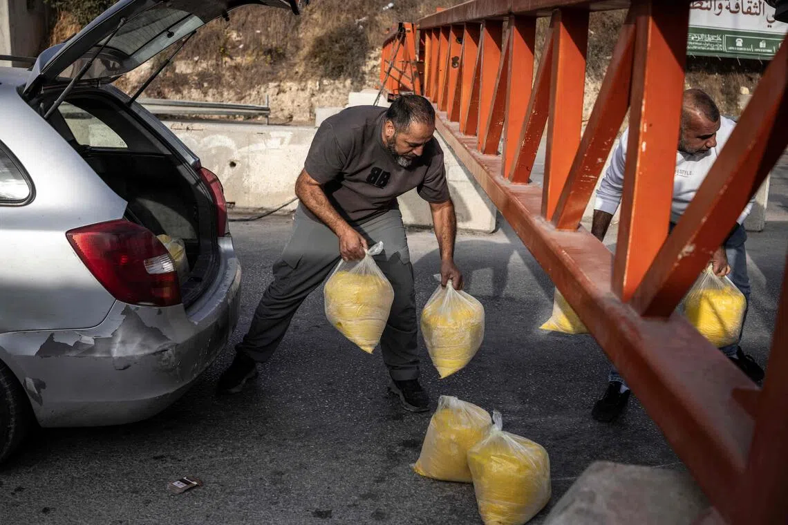 People pass packages under a closed checkpoint gate to the Israeli occupied West Bank city of Hebron on Oct 24.