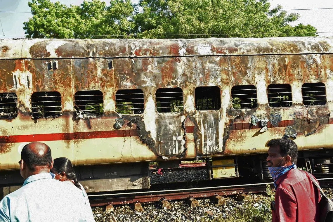 People walk past a damaged train coach parked at the Madurai railway yard after a fire broke out in the early hours of the morning, in Madurai on August 26, 2023. At least nine people were killed on August 26, after a train coach parked in southern India caught fire when a passenger tried to make tea, officials said. (Photo by AFP)