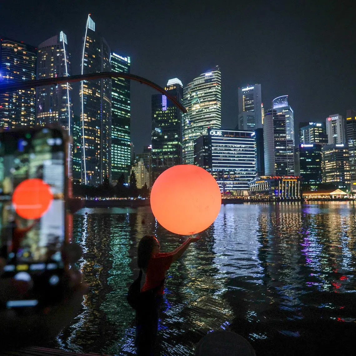 iLight Singapore 2026 media preview - Passers-by experiencing an installation by Chinese artist Wentao Wang called “Let’s Fish The Sun”, at the Marina Bay Lower Boardwalk, on June 3, 2026. The piece involves a fishing rod extending over the water, suspending a luminous orb hovering just above the surface. It is one of a series of installations for i Light Singapore, which opens on June 5. 
