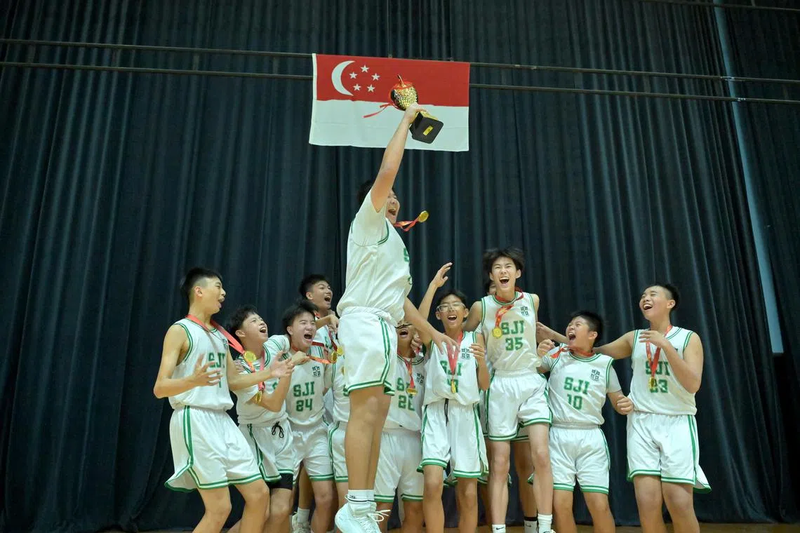 St Joseph's Institution captain Jude Ng hoists the C Division boys' basketball trophy as his team celebrates a 57-47 win over Presbyterian High School in the final.