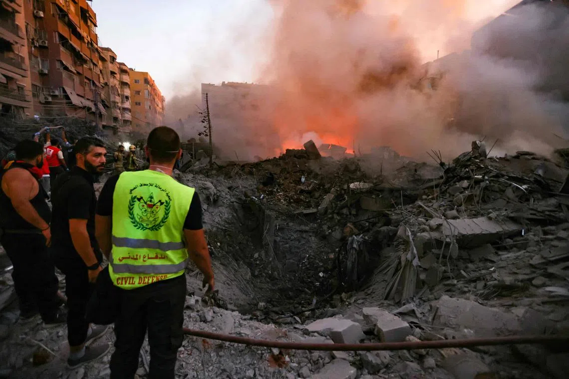 People and rescuers gather near the smouldering rubble of a building destroyed in an Israeli air strike in Beirut's southern suburbs on Sept 27.