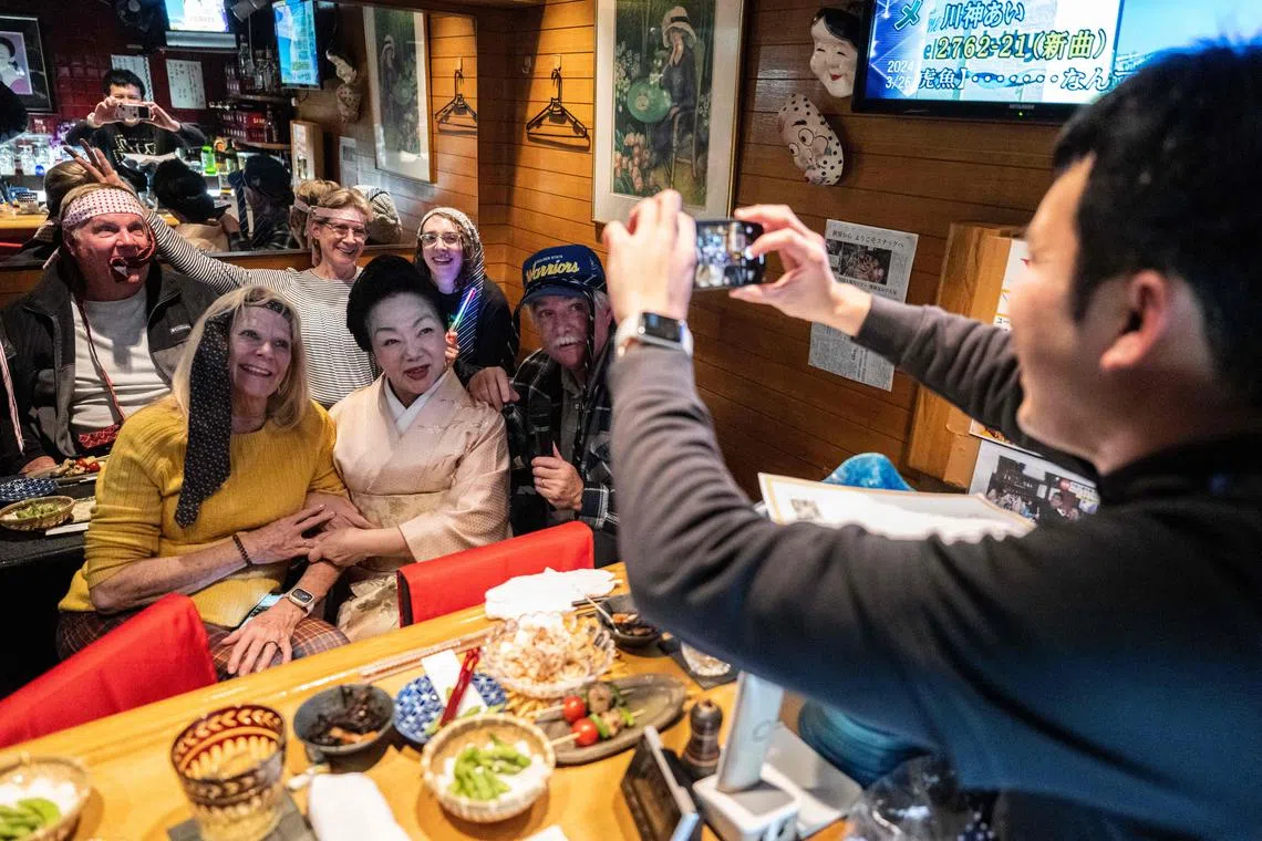 This picture taken on March 22, 2024 shows tourists posing for a picture with "mama-san" Kuri Awaji (C), who runs a snack bar, during a snack bar tour at her bar "Kuriyakko" in Tokyo. Snack bars are cosy, retro establishments found across Japan, often crammed into small buildings and equipped with karaoke systems that echo late into the night. (Photo by Yuichi YAMAZAKI / AFP) / TO GO WITH Japan-lifestyle-culture-tourism,FOCUS by Katie FORSTER