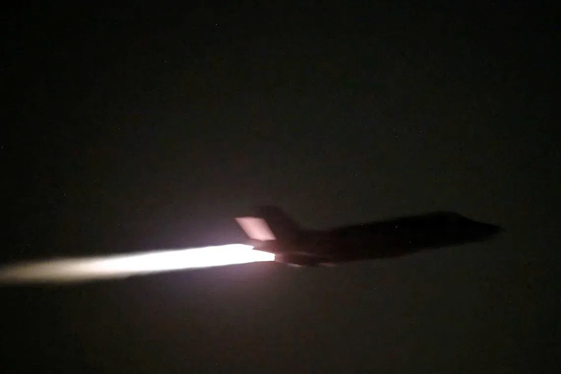 Silhouette of an airplane flying at night with a bright light emanating from its front.