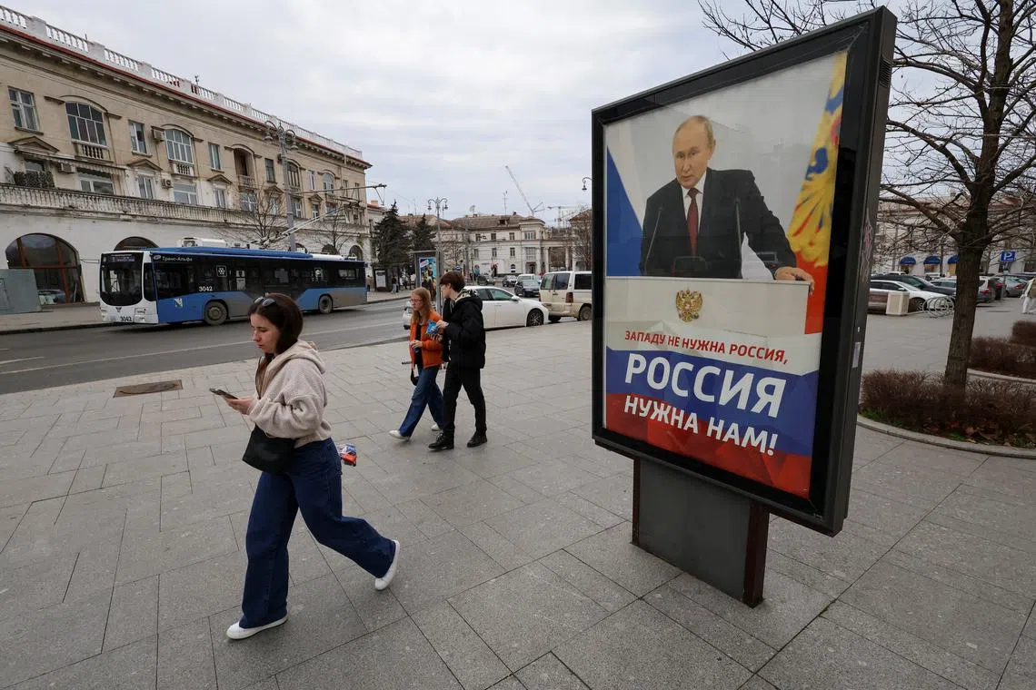 Pedestrians walk past a poster displayed in support of Russia's President Vladimir Putin in a street in the Black Sea port of Sevastopol, Crimea, February 14, 2024. A slogan on the poster reads: \"Russia is not needed for the West, Russia is needed for us! REUTERS/Alexey Pavlishak/File Photo