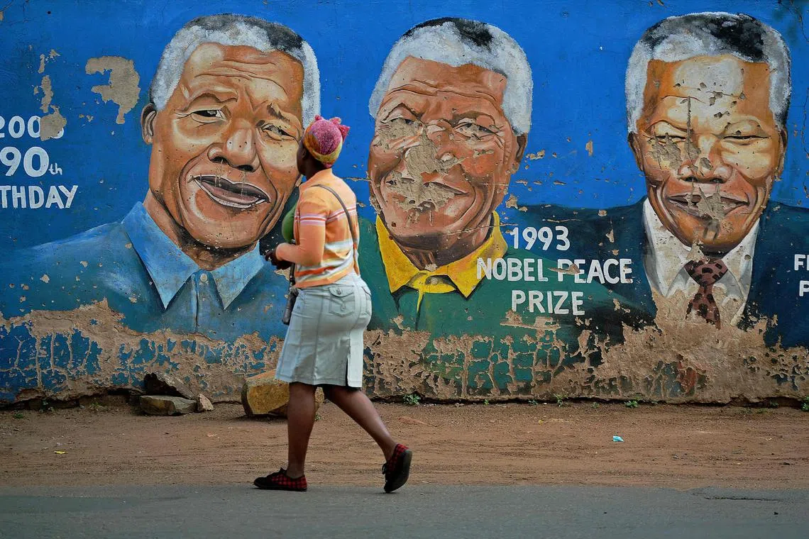 (FILES) Residents walk past murals of late South African former president Nelson Mandela in Soweto, near Johannesburg, on December 7, 2013, two days after his death. Anti-apartheid hero Nelson Mandela has been seen as a moral compass in his home South Africa, but ten years after his death his legacy is vigorously debated, with some questioning the quality of the country's democracy. (Photo by Carl DE SOUZA / AFP)