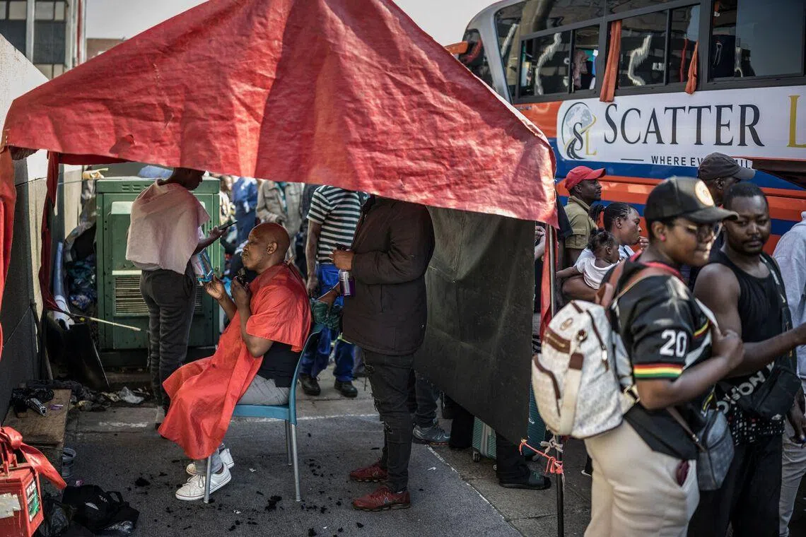 TOPSHOT - A man trims his beard at a roadside barber shop as undocumented migrants, mostly Zimbabwean, Malawians and Mozambicans, gather at the Cartwright Old Taxi Rank before boarding a bus heading to Zimbabwe in Durban, on June 28, 2026. South Africans President Cyril Ramaphosa vowed on Thursday to crush any attempts to destabilise the nation during planned anti-immigrant marches next week, amid a wave of xenophobia. Citizen-led groups have set Tuesday 30 as a deadline for undocumented foreigners to leave and called for nationwide marches against illegal immigration, marking a crescendo in months of protests that have at times turned violent. (Photo by MARCO LONGARI / AFP)