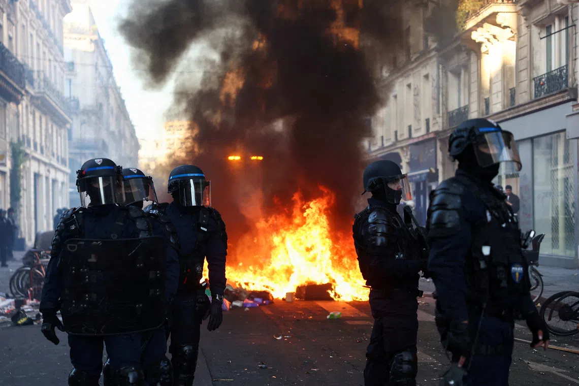 A fire burns as Police officers in riot gear stand guard during civil unrest in Paris, France on Oct 18.