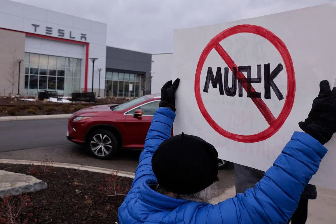 A person holds up a sign during a protest against Elon Musk outside of a Tesla dealership in Michigan, US, on Feb 27, 2025. 