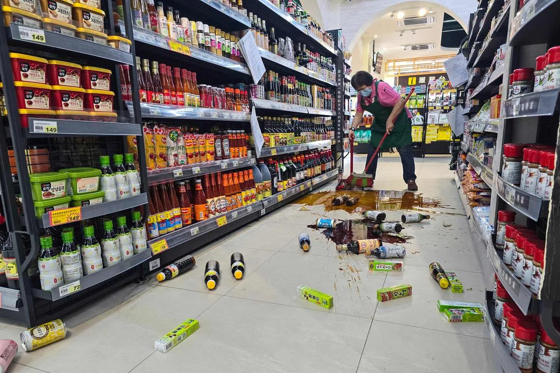 An employee clearing broken bottles on the floor of a supermarket in Yilan, following a major earthquake in eastern Taiwan on April 3, 2024.