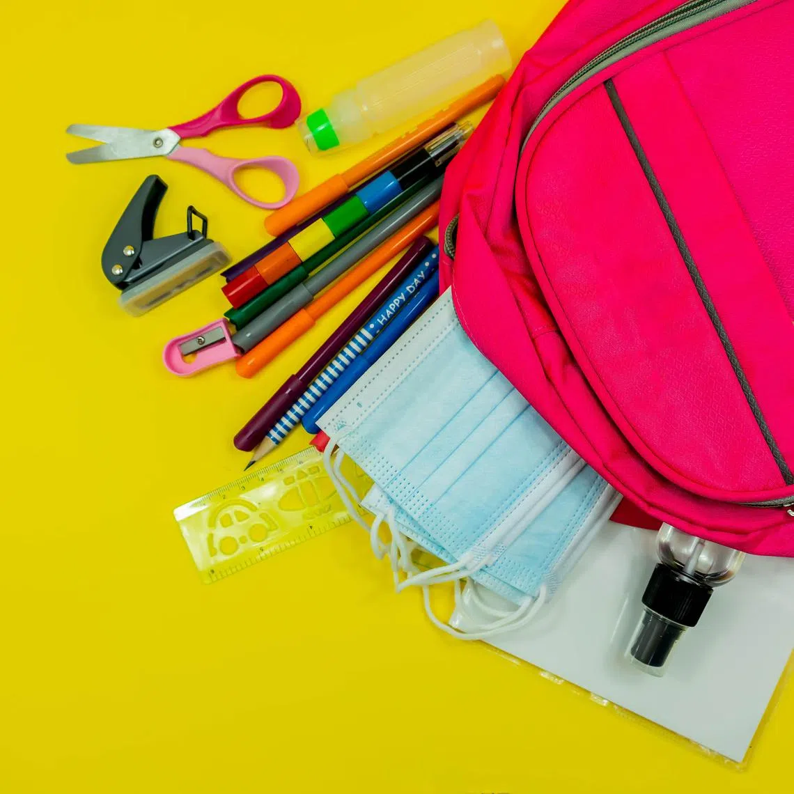 School supplies like pencil scissor eraser ruler watercolor mask alcohol sanitizer inside a pink bag backpack on yellow background. Back to school concept during covid pandemic with copy space